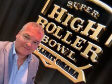 Ein Mann in einem schwarzen Anzug und einer dunklen Sonnenbrille sitzt an einem Pokertisch und betrachtet seine Karten während eines High-Stakes Pot-Limit Omaha-Turniers.