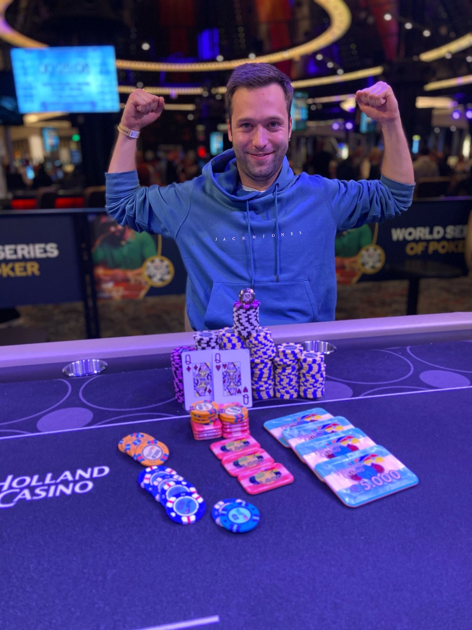 Ein Bild eines Pokertisches mit Spielkarten und Pokerchips, umgeben von Personen, die Poker spielen.