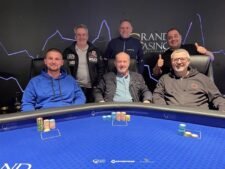 Ein Poker-Turniertisch mit grünen Filz und Chips, auf denen das Progressive Bounty-Logo zu sehen ist. Es liegen Karten und Dealer-Buttons auf dem Tisch, der von Spielern umgeben ist.