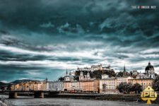 Ein atemberaubendes Panorama von Salzburg mit der Festung Hohensalzburg und der malerischen Altstadt, umgeben von grünen Hügeln und einem blauen Himmel.