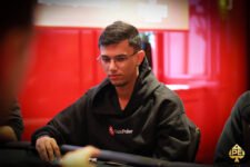 Ein junger Mann namens Samuel Mullur sitzt an einem Pokertisch, hält Karten in der Hand und lächelt selbstbewusst in die Kamera.