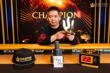 Ein Mann in einem dunklen Anzug und einer Sonnenbrille, der jubelnd die Hände in die Luft wirft, umgeben von einer Menschenmenge in einem Casino. Im Hintergrund sind Pokertische und Spieler zu