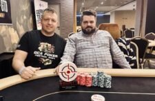 Ein Mann und eine Frau sitzen an einem Pokertisch mit Chips und Karten. Der Mann hat eine Hand am Kinn und schaut nachdenklich, während die Frau lächelnd ihre Karten betrachtet.