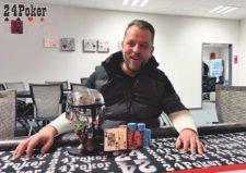 Ein Gruppenfoto von Pokerspielern, die lächelnd und jubelnd ihre Hände in die Luft strecken. In der Mitte steht ein Spieler mit einem großen Pokal in der Hand.