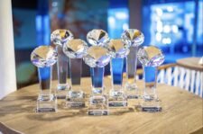 Ein bunter und lebendiger Pokertisch mit Spielkarten, Pokerchips und einem gemischten Stapel von Spielkarten, umgeben von vier Personen, die konzentriert und fokussiert auf ihre K