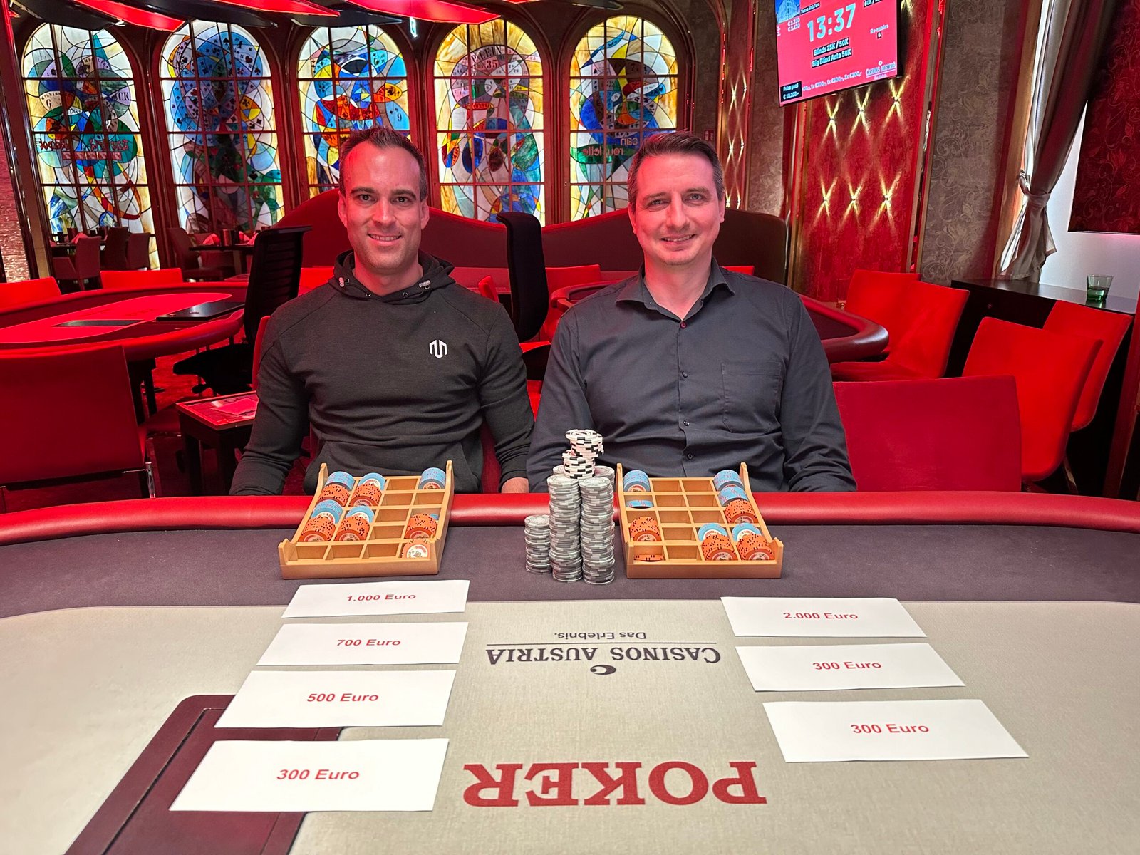 Ein Mann und eine Frau sitzen an einem Pokertisch und spielen Texas Hold'em. Die Frau hält zwei Karten in der Hand und schaut konzentriert auf den Tisch, während der Mann Pokerchips stapelt. Die