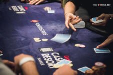Ein Mann sitzt an einem Pokertisch und betrachtet konzentriert seine Karten. Im Hintergrund sind andere Spieler und Spielchips zu sehen.