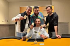 Ein Mann mit dunklen Haaren und einem dunklen Anzug sitzt an einem Pokertisch und schaut konzentriert auf seine Karten.