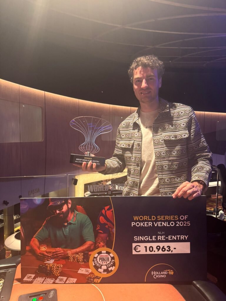 Ein Mann in einem dunklen Anzug und einer roten Krawatte sitzt an einem Pokertisch mit grüner Filzdecke. Er hält zwei Spielkarten in der Hand und schaut konzentriert auf seine