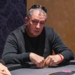 Ein Mann sitzt an einem Pokertisch und studiert konzentriert seine Karten. Um ihn herum befinden sich Pokerchips und Spielkarten.