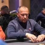 Ein Mann sitzt an einem Pokertisch mit einer Hand voll Spielkarten, während er konzentriert auf seine Gegner schaut.