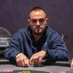 Ein Mann und eine Frau sitzen an einem Pokertisch und spielen gegeneinander. Der Mann hat einen ernsten Gesichtsausdruck und hält Karten in der Hand, während die Frau konzentriert ihre Karten