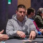 Ein grüner Pokertisch mit Spielkarten, Pokerchips und Getränken, umgeben von vier Personen, die Poker spielen und lächeln.
