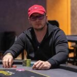 Ein Mann sitzt an einem Pokertisch, umgeben von Spielkarten und Pokerchips. Er betrachtet konzentriert seine Karten und den Pot in der Mitte des Tisches.
