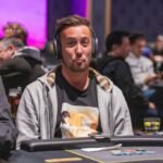 Ein Mann und eine Frau sitzen lächelnd an einem Pokertisch. Der Mann hält Karten in der Hand und die Frau schaut ihn interessiert an. Im Hintergrund sind Pokerchips und Getränke zu