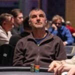 Ein Mann und eine Frau sitzen an einem Pokertisch, beide konzentriert auf ihre Karten. Die Frau hat blonde Haare und trägt ein rotes Oberteil, während der Mann dunkle Haare und ein weißes