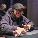 Ein Mann und eine Frau sitzen an einem Pokertisch und spielen Texas Hold'em. Der Mann hat eine Hand mit Karten in der Hand und schaut konzentriert auf den Tisch, während die Frau mit einem Pokerchip spielt
