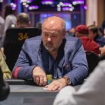 Ein Mann sitzt an einem Pokertisch und hält Karten in der Hand, während er konzentriert auf seine Gegner schaut.