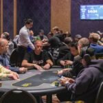Ein Mann und eine Frau spielen Poker in einem eleganten Casino. Der Mann hat einen Stapel Chips vor sich und schaut konzentriert auf seine Karten, während die Frau lächelnd ihre Karten betrachtet. Die Sz