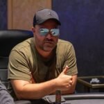 Ein Mann und eine Frau sitzen an einem Pokertisch und spielen Texas Hold'em. Der Mann hält Karten in der Hand, während die Frau mit ernstem Gesichtsausdruck auf ihre Chips schaut. Eine Stapel von