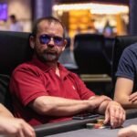 Ein Bild von vier Pokerspielern an einem Tisch mit Pokerchips und Karten. Zwei Männer und zwei Frauen konzentrieren sich auf ihre Hände und betrachten ihre Karten. Die Spannung und Konkurrenz