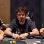 Ein Mann und eine Frau spielen Poker an einem Tisch in einem eleganten Casino. Der Mann hat Karten in der Hand und konzentriert sich auf das Spiel, während die Frau mit einem selbstbewussten Blick ihre Karten betracht