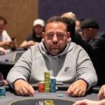 Ein Mann und eine Frau sitzen an einem Pokertisch und spielen Texas Hold'em. Der Mann hat eine Hand mit Karten und Chips vor sich, während die Frau konzentriert ihre Karten betrachtet. Im Hintergrund sind