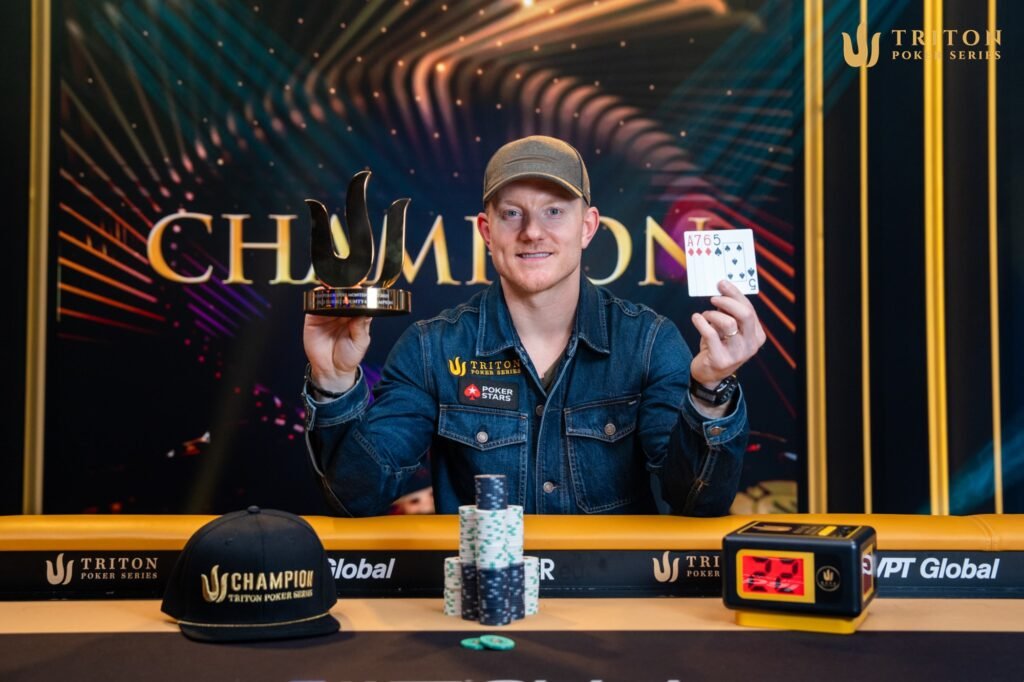 Ein Mann in einem dunklen Anzug und mit kurzem Haar sitzt an einem Pokertisch, umgeben von Spielkarten und Pokerchips. Er schaut konzentriert auf seine Karten und hat eine ernste Mi