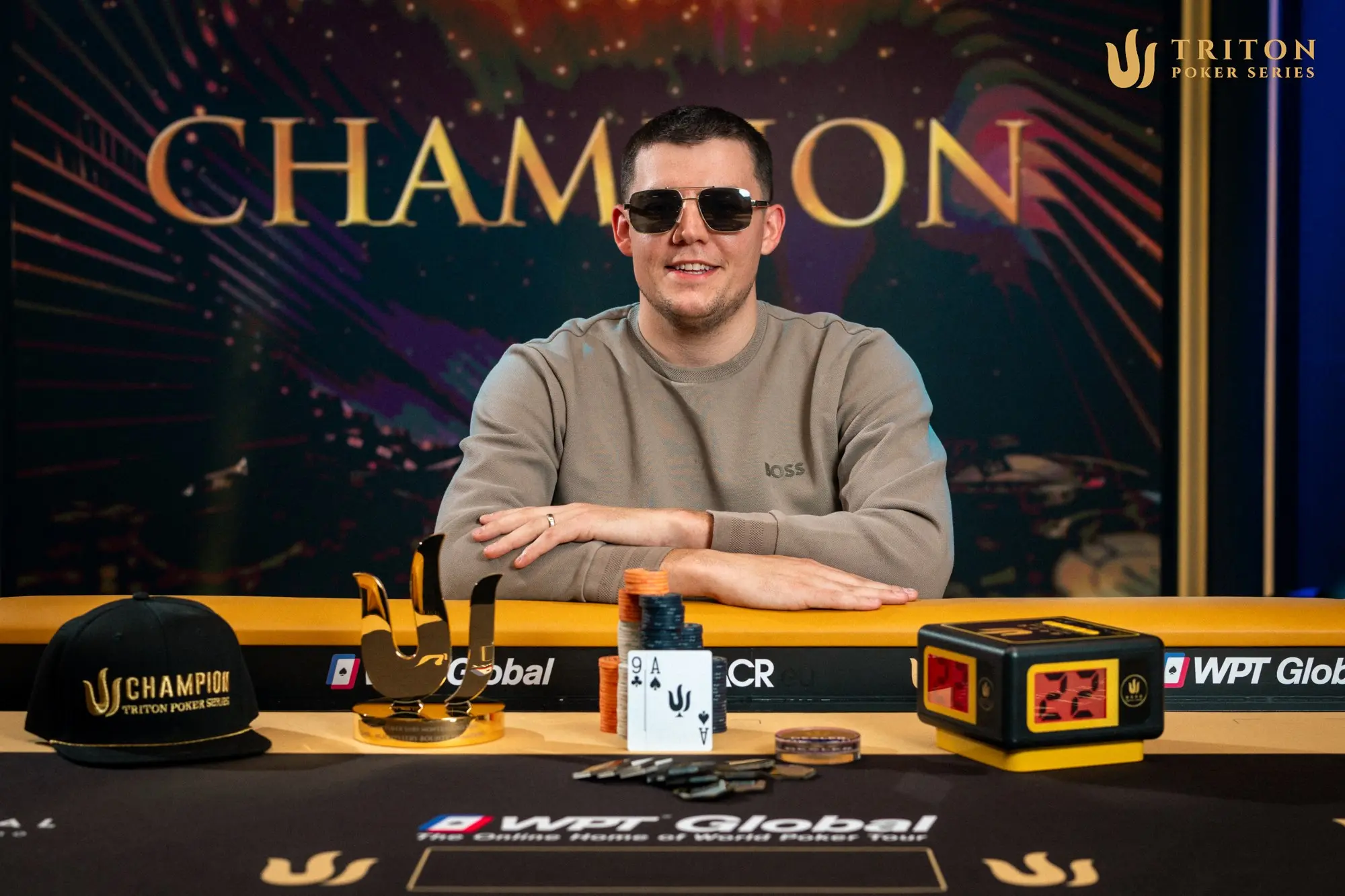Ein Mann in einem dunklen Anzug und einer Sonnenbrille hält einen riesigen Pokal in die Luft, umgeben von jubelnden Menschen.