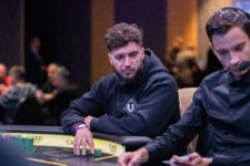 Ein Mann mit dunklen Haaren und einem schwarzen Hemd, der konzentriert Poker spielt. Er sitzt an einem Pokertisch mit Chips und Karten vor sich.