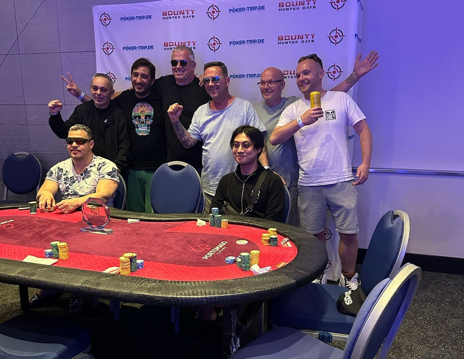 Ein Mann und eine Frau sitzen an einem Pokertisch und spielen eine Partie Poker. Der Mann hat eine Hand mit Spielkarten in der Hand, während die Frau konzentriert auf ihre Karten schaut. Im Hintergrund
