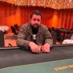 Ein Tisch mit Pokerchips, Karten und Getränken, umgeben von vier Personen, die konzentriert Poker spielen.