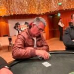 Ein professioneller Pokertisch mit grünem Filz, umgeben von Stühlen und Chips. Zwei Spieler mit Karten in der Hand sind konzentriert auf ihr Spiel. Die Spannung ist spürbar.