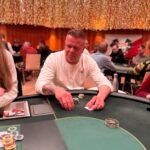 Ein professioneller Pokertisch mit grünem Filz, umgeben von Spielkarten, Pokerchips und Getränken. Vier Personen sitzen um den Tisch herum und konzentrieren sich auf ihre Karten