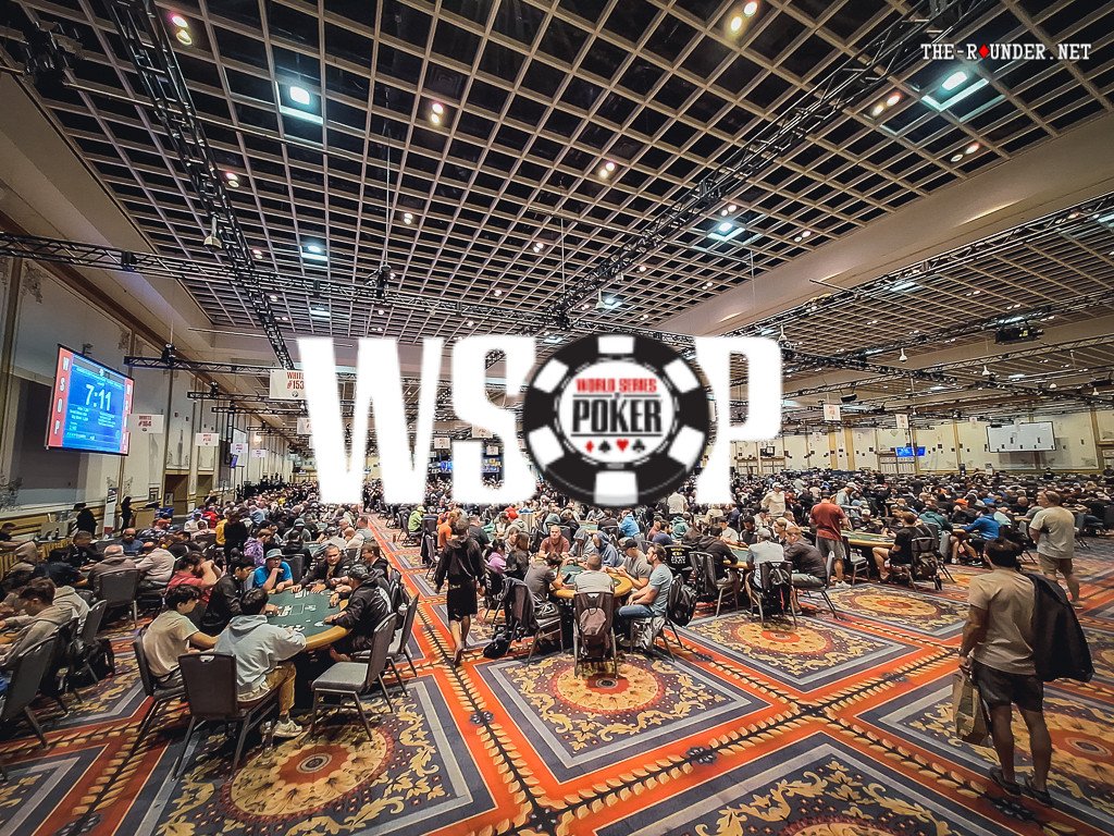 Ein Mann sitzt an einem Pokertisch während eines Turniers der World Series of Poker. Er hat eine Hand mit Karten in der Luft und konzentriert sich auf das Spielgeschehen.