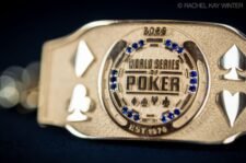 Ein professioneller Pokertisch mit grünen Filz, umgeben von schwarzen Lederstühlen. In der Mitte des Tisches liegen Pokerchips und Spielkarten. Im Hintergrund sind Spieler in gedä