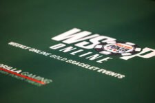 Ein professioneller Pokerspieler mit Sonnenbrille und Kappe sitzt an einem Tisch während des World Series of Poker-Turniers. Er hält Karten in der Hand und betrachtet konzentriert seine Gegner