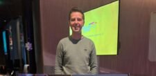Ein professioneller Pokerspieler mit Sonnenbrille und Kappe sitzt an einem grünen Pokertisch, umgeben von anderen Spielern. Die Karten und Chips liegen vor ihm, während er konzentriert seine