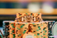 Ein Mann in einem schwarzen Anzug sitzt an einem Pokertisch und hält stolz ein goldenes Armband, das er bei der World Series of Poker (WSOP) gewonnen hat.