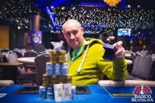 Ein Mann sitzt an einem Pokertisch in einem Casino, umgeben von anderen Spielern. Er hält mit ernstem Gesichtsausdruck Karten in der Hand und betrachtet sie konzentriert. Die Atmosph