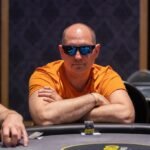 Ein Mann und eine Frau sitzen am Pokertisch und spielen eine Partie Poker. Der Mann hat eine Hand Karten in der Hand und schaut konzentriert auf den Tisch, während die Frau ihre Karten ansieht.