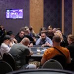 Ein stilvolles Pokerspiel mit einer Gruppe von Personen, die um einen Tisch herum sitzen und Karten halten. Die Spieler sind konzentriert und in Gedanken versunken, während sie ihre Strategien planen.