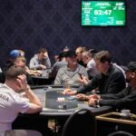 Ein Mann und eine Frau sitzen an einem Pokertisch und spielen Karten. Der Mann hält seine Karten verdeckt, während die Frau ihre Karten betrachtet. Im Hintergrund sind Pokerchips und Geträn