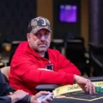 Ein professioneller Pokertisch mit grünem Filz, umgeben von Pokerspielern, die Karten halten und Chips stapeln. Ein Spieler hat gerade eine Hand gewonnen und jubelt.