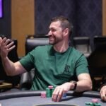 Ein Mann und eine Frau sitzen an einem Pokertisch, konzentriert auf ihre Karten und Chips. Die Frau hat eine Hand am Kinn und schaut nachdenklich, der Mann hat seine Hand am Kopf und wir