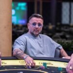 Ein Mann und eine Frau sitzen an einem Pokertisch und halten Karten in der Hand. Sie haben konzentrierte Gesichtsausdrücke und scheinen ein intensives Pokerspiel zu spielen. Die Frau hat lange dunk