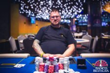 Ein Pokertisch mit grünem Filz, umgeben von Spielkarten, Jetons und einem Dealer-Button. Mehrere Hände von Spielern sind sichtbar, die ihre Karten halten. Es herrscht eine span