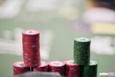 Ein Stapel von bunten Pokerchips auf einem grünen Tisch, der während der World Series of Poker platziert ist. Ein Spieler ist im Hintergrund zu sehen, der seine Karten betrachtet.