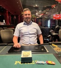 Ein Mann und eine Frau sitzen an einem Pokertisch und spielen eine Runde Poker. Der Mann hält Karten in der Hand, während die Frau konzentriert auf ihre Karten schaut. Der Tisch ist mit Pokerch